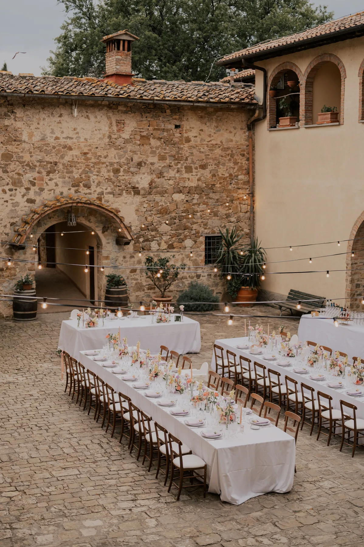 Longue tablée dressée dans une cour en pierre, décoration de mariage signée Mona Ilsa