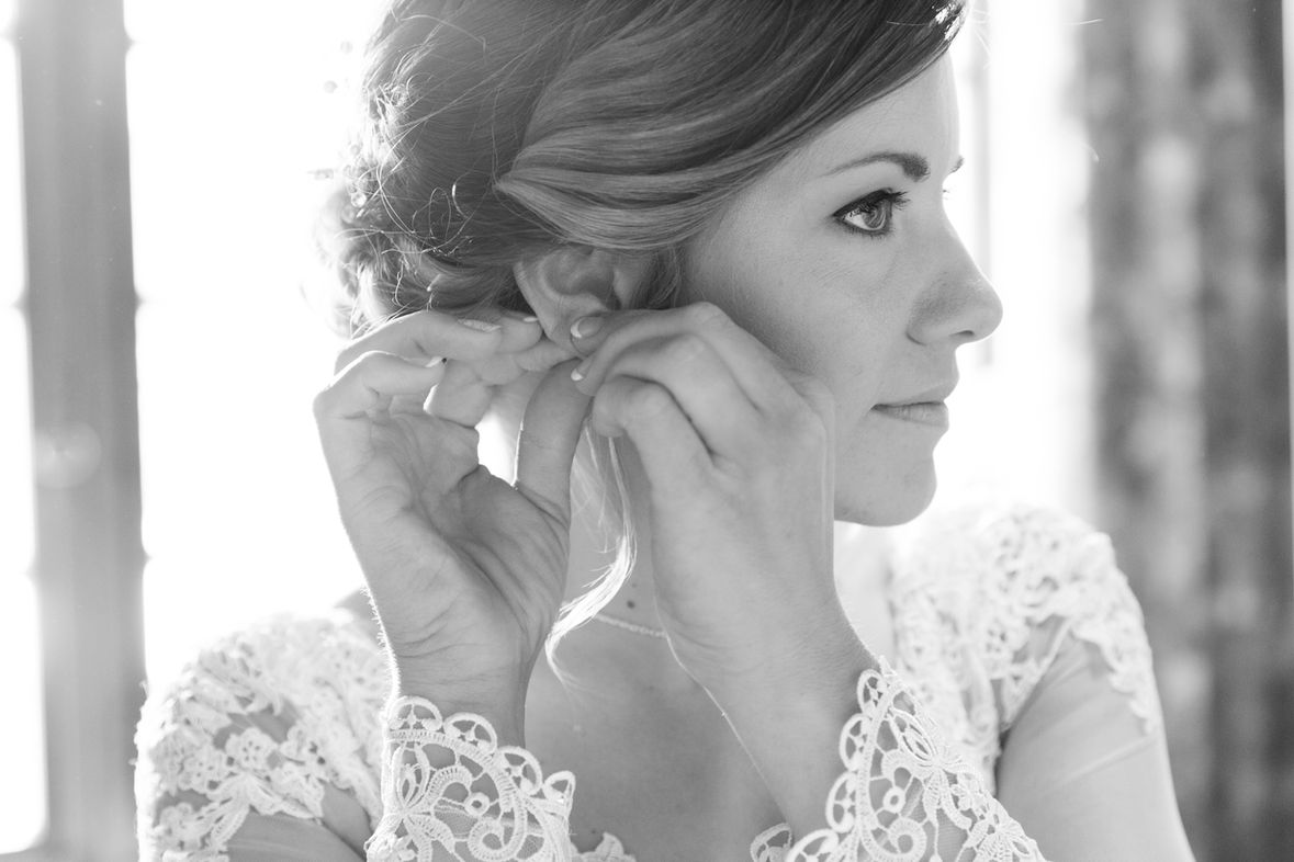 La mariée met ses boucles d'oreilles pendant les préparatifs, en noir et blanc