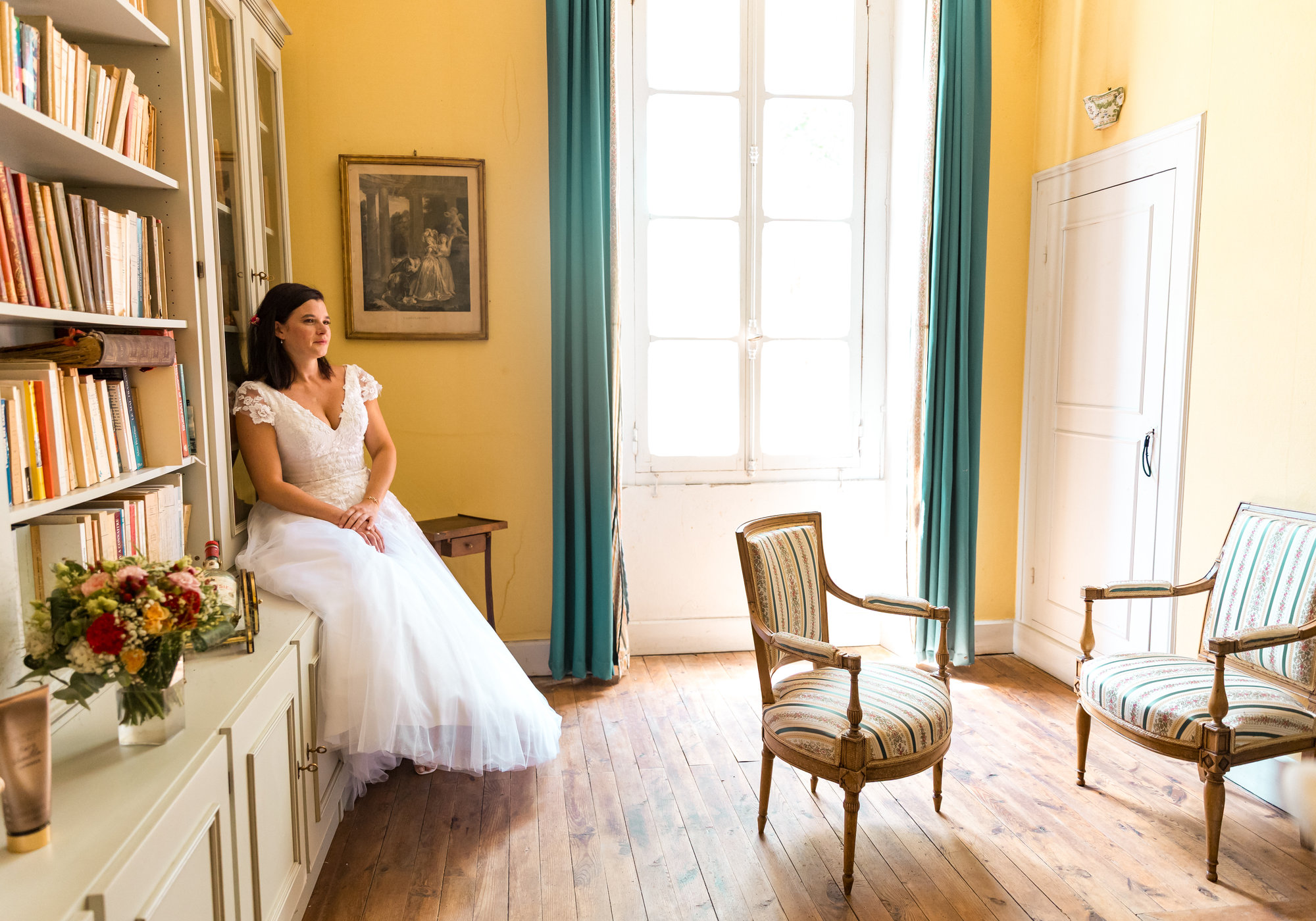 La mariée assise près de la fenêtre d'un salon aux murs jaunes