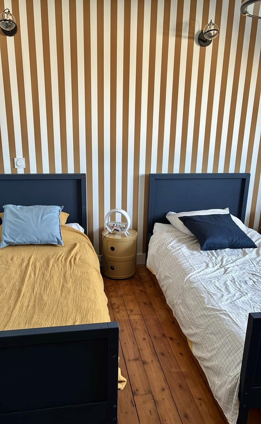 Chambre de jumeaux : lits repeints en bleu marine devant un papier peint rayé moutarde