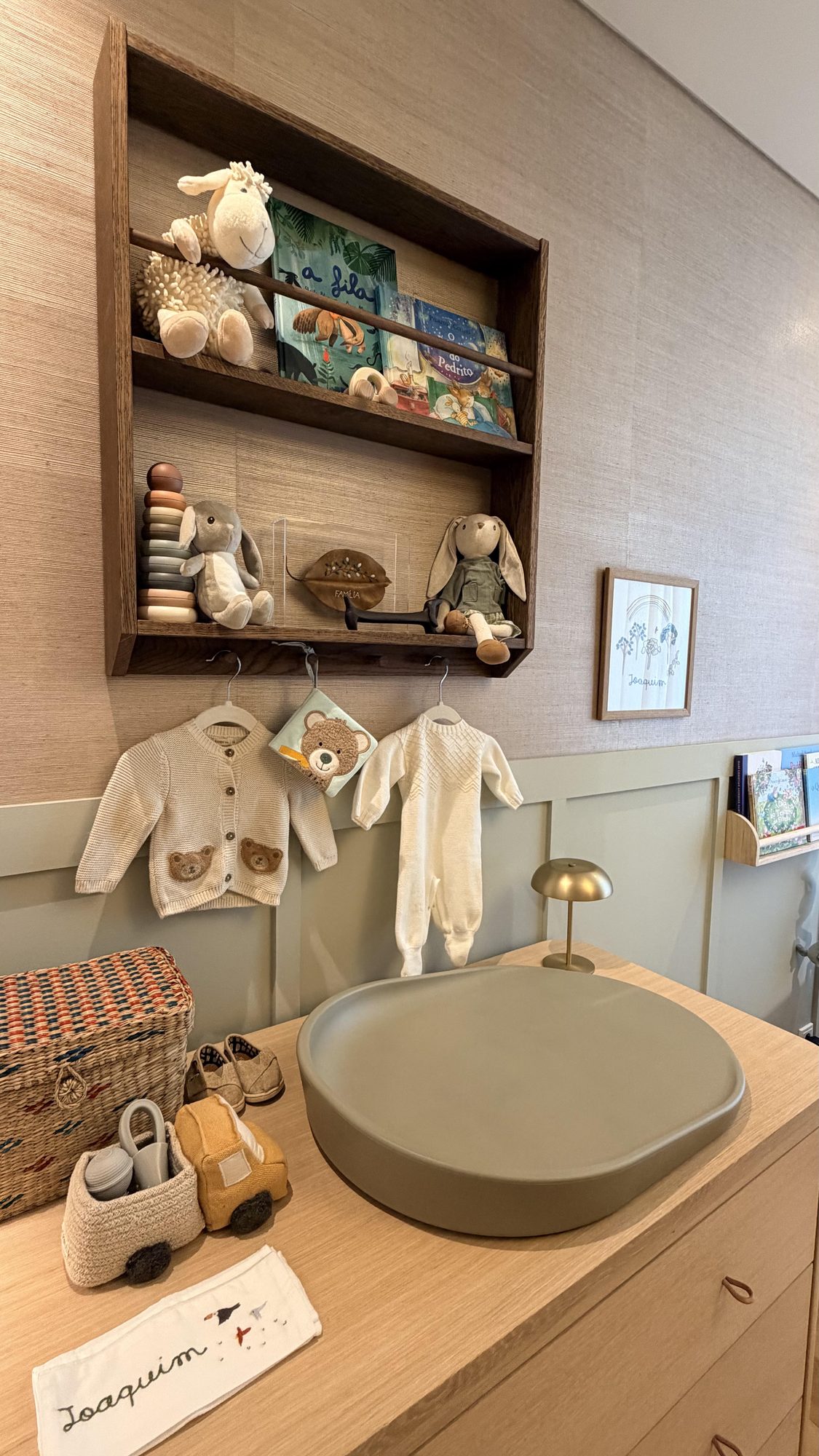 Étagère en bois foncé au-dessus de la commode : peluches, livres, petits vêtements et cadre au prénom de Joaquim